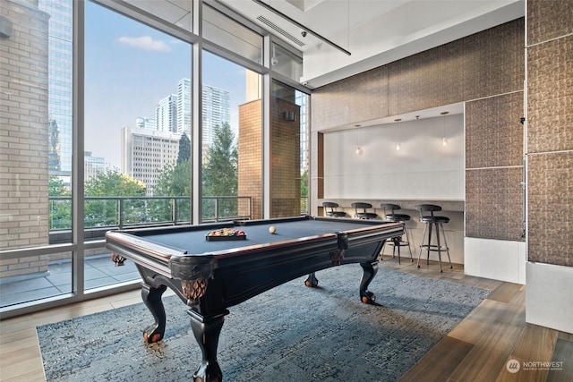 game room with expansive windows, a towering ceiling, a healthy amount of sunlight, and wood-type flooring