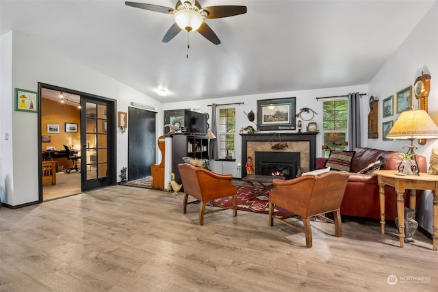 living area featuring ceiling fan, lofted ceiling, a fireplace, and light hardwood / wood-style flooring