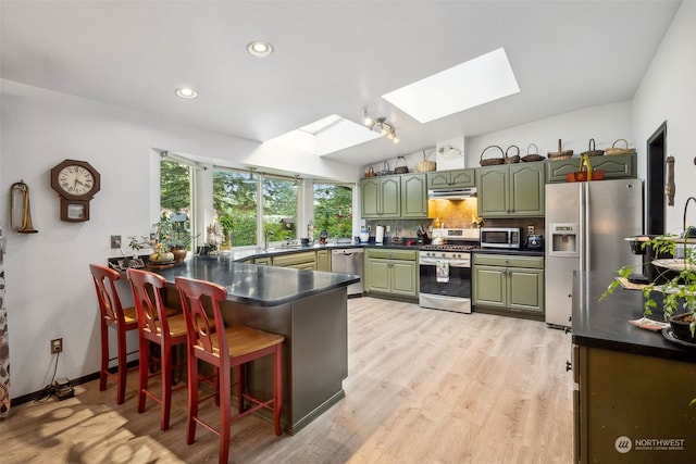 kitchen featuring light wood-type flooring, lofted ceiling with skylight, green cabinetry, stainless steel appliances, and kitchen peninsula