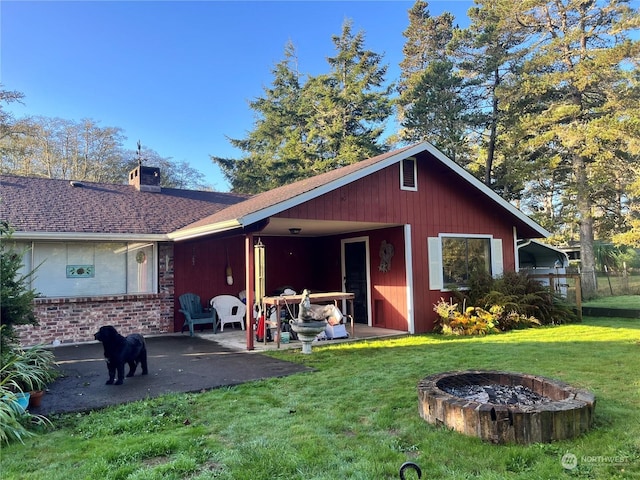 rear view of house with an outdoor fire pit, a chimney, a yard, and a patio