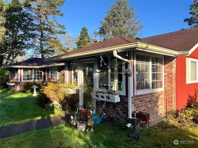 view of front of property with a sunroom, a front yard, roof with shingles, and brick siding