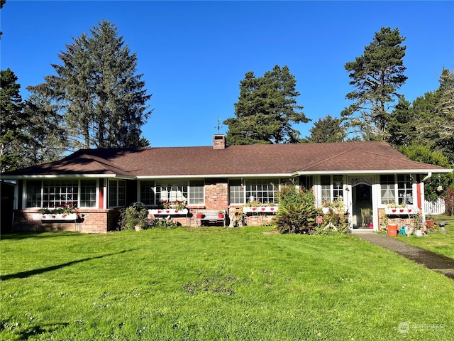 view of front facade featuring a chimney, brick siding, a front yard, and roof with shingles