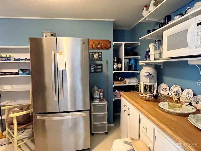 kitchen featuring white cabinets, open shelves, freestanding refrigerator, white microwave, and butcher block countertops