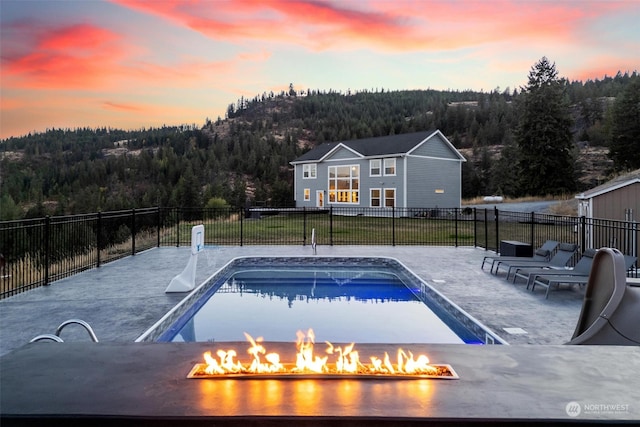 pool at dusk featuring an outdoor fire pit and a lawn