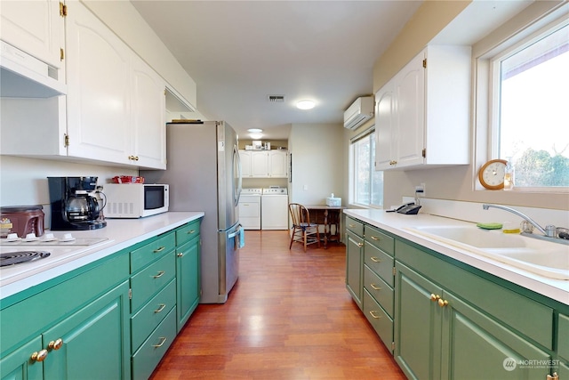 kitchen featuring washer and dryer, a wall mounted air conditioner, sink, white cabinets, and plenty of natural light