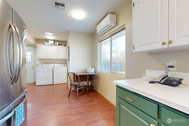 kitchen featuring washing machine and clothes dryer, white cabinetry, a wall mounted AC, light wood-type flooring, and stainless steel fridge