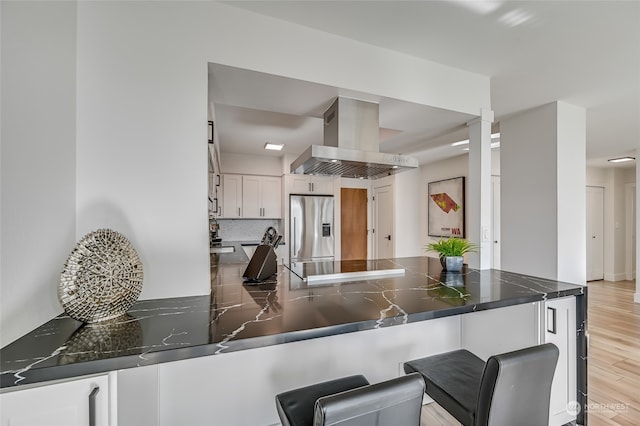 kitchen featuring island exhaust hood, light hardwood / wood-style flooring, backsplash, stainless steel fridge, and white cabinetry