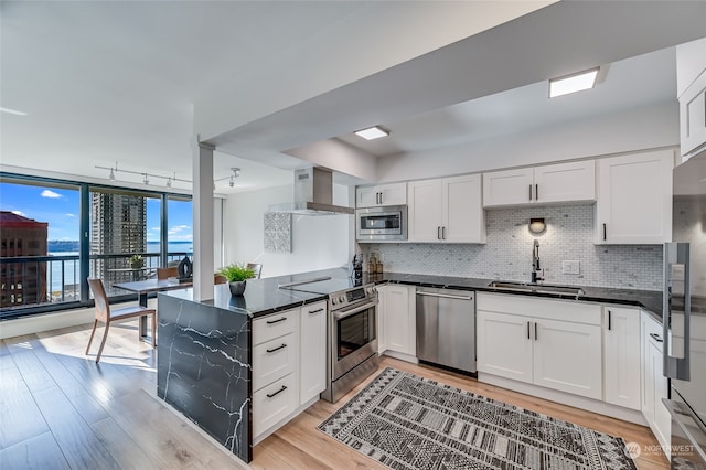 kitchen featuring sink, appliances with stainless steel finishes, wall chimney range hood, and white cabinetry