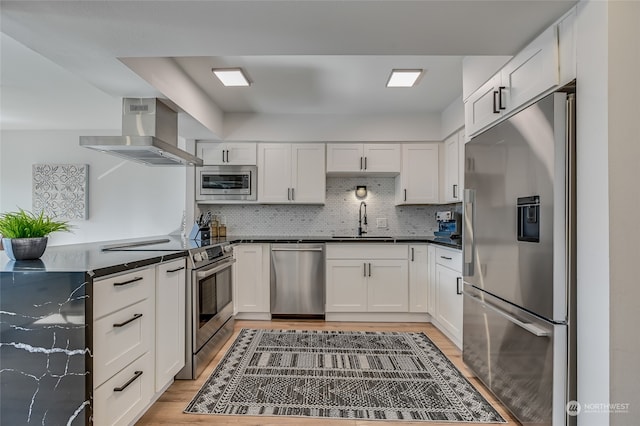 kitchen featuring wall chimney range hood, white cabinets, stainless steel appliances, and sink