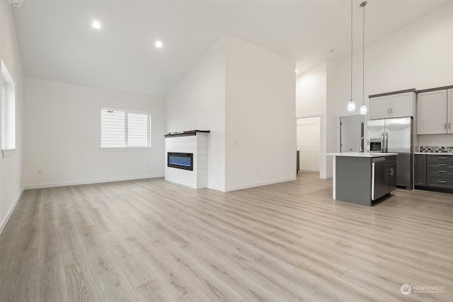 unfurnished living room featuring high vaulted ceiling, sink, and light hardwood / wood-style floors