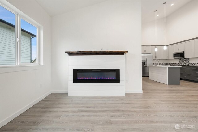 unfurnished living room featuring high vaulted ceiling, sink, and light wood-type flooring