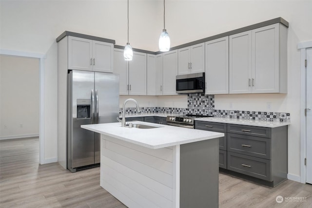 kitchen featuring decorative light fixtures, sink, an island with sink, gray cabinetry, and stainless steel appliances