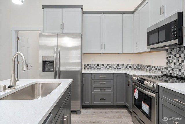 kitchen featuring light stone countertops, stainless steel appliances, sink, gray cabinets, and light hardwood / wood-style flooring