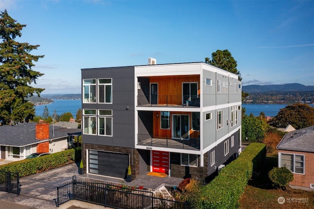 exterior space with a balcony, an attached garage, driveway, and a water view