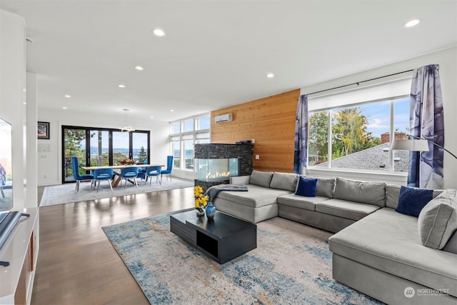 living room with recessed lighting, wooden walls, a multi sided fireplace, and wood finished floors