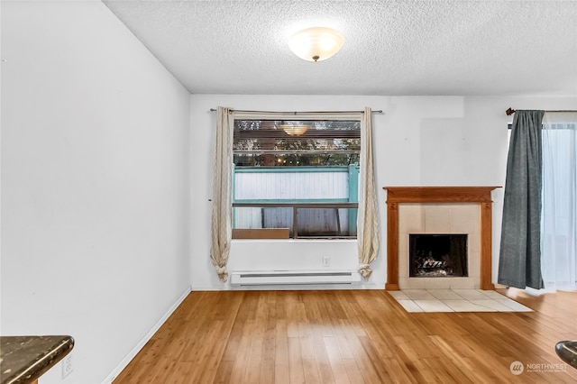 unfurnished living room featuring a textured ceiling, a tile fireplace, light hardwood / wood-style floors, and baseboard heating