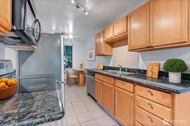 kitchen featuring sink, light tile patterned floors, rail lighting, stainless steel dishwasher, and dark stone counters