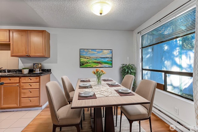 dining space featuring sink, a textured ceiling, baseboard heating, and light hardwood / wood-style flooring