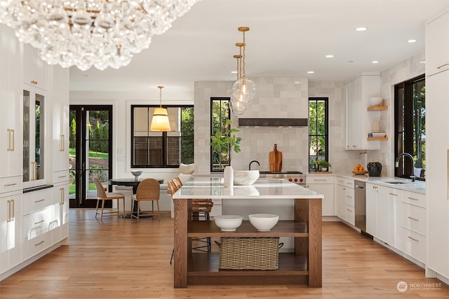 kitchen with wall chimney exhaust hood, light hardwood / wood-style floors, white cabinetry, and hanging light fixtures