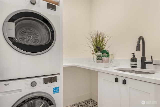 clothes washing area with cabinets, sink, and stacked washer / dryer