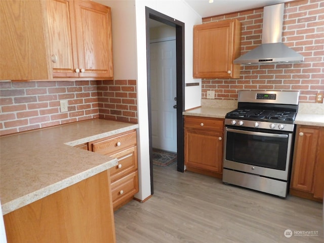 kitchen with light wood-type flooring, wall chimney exhaust hood, decorative backsplash, and gas range