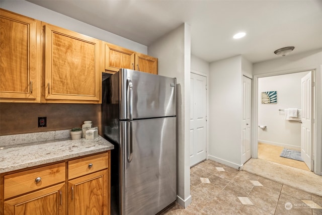 kitchen with light stone counters, stainless steel refrigerator, and light tile patterned floors