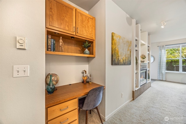 office area featuring built in desk, a fireplace, and light colored carpet