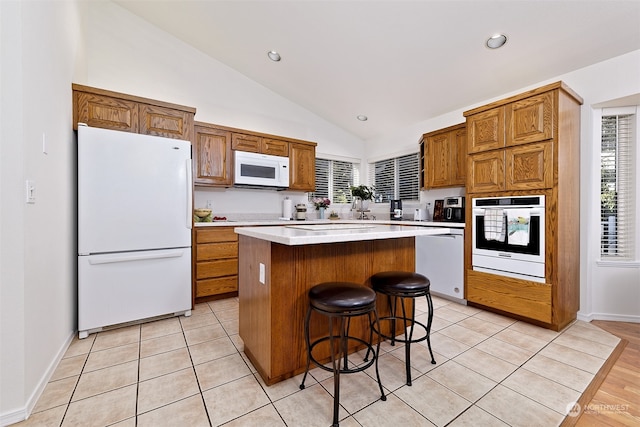 kitchen with light tile patterned flooring, white appliances, a center island, a breakfast bar, and vaulted ceiling