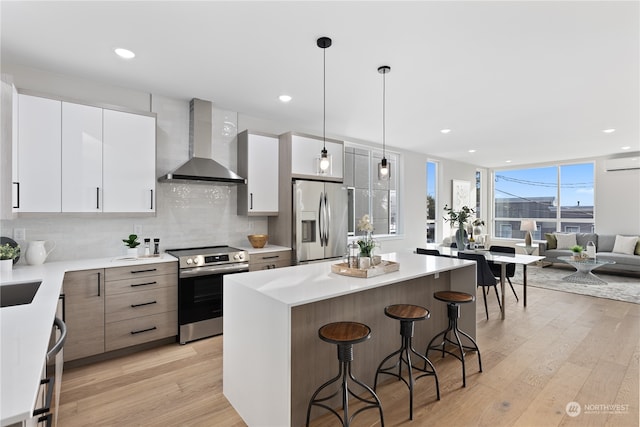 kitchen featuring white cabinets, appliances with stainless steel finishes, wall chimney exhaust hood, and light hardwood / wood-style floors