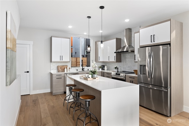 kitchen with appliances with stainless steel finishes, wall chimney range hood, white cabinetry, and a center island