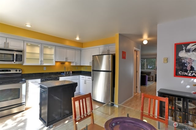 kitchen with white cabinetry, sink, stainless steel appliances, dark stone counters, and a kitchen island