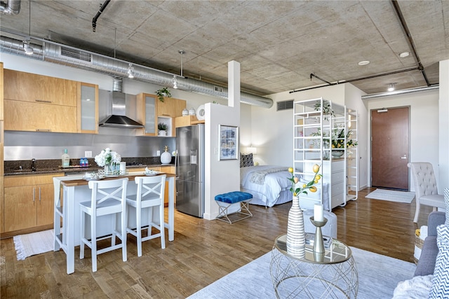 kitchen featuring a kitchen island, stainless steel fridge, hardwood / wood-style flooring, wall chimney range hood, and a breakfast bar area