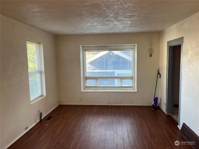 spare room featuring plenty of natural light, dark wood-type flooring, and a textured ceiling