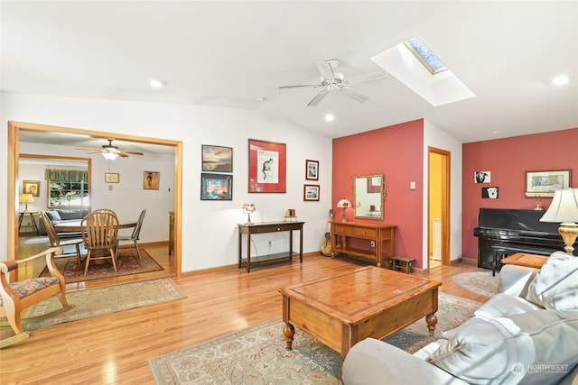 living room featuring ceiling fan, lofted ceiling with skylight, and light hardwood / wood-style floors