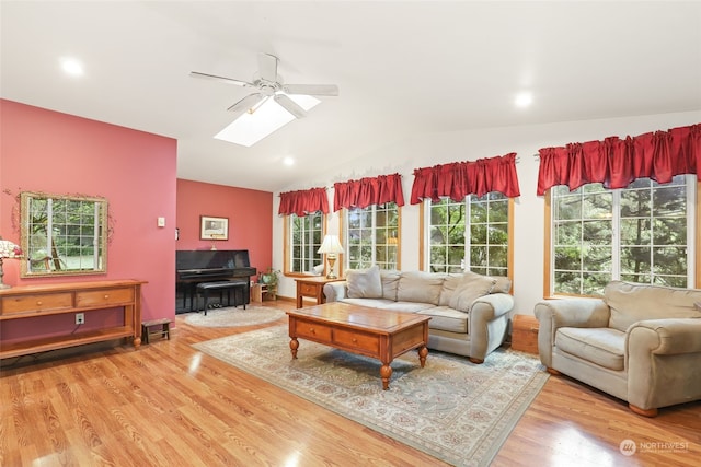 living room with light wood-type flooring, ceiling fan, and vaulted ceiling with skylight