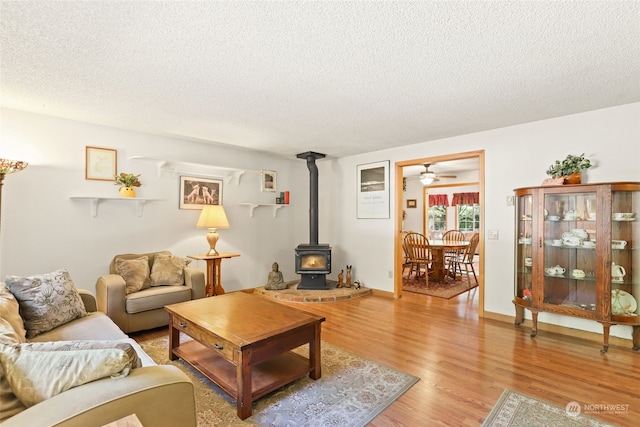 living room featuring ceiling fan, hardwood / wood-style flooring, a textured ceiling, and a wood stove