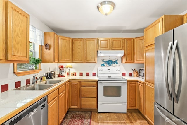 kitchen featuring sink, appliances with stainless steel finishes, tile counters, light wood-type flooring, and decorative backsplash