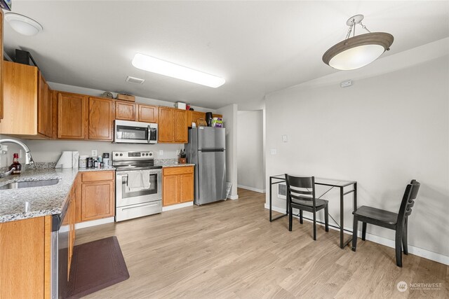 kitchen with light stone counters, pendant lighting, sink, stainless steel appliances, and light hardwood / wood-style floors