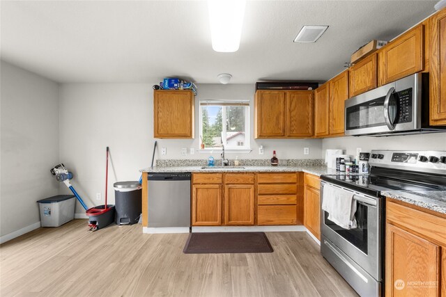 kitchen with appliances with stainless steel finishes, sink, and light hardwood / wood-style flooring