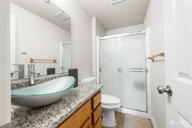 bathroom featuring wood-type flooring, a shower with shower door, vanity, and toilet