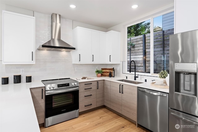 kitchen featuring white cabinets, appliances with stainless steel finishes, wall chimney exhaust hood, and sink