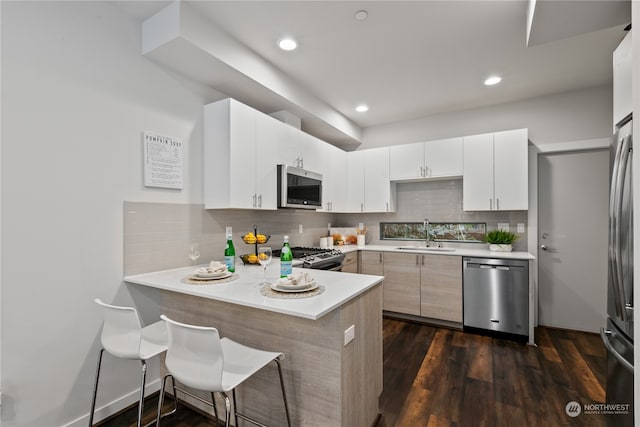 kitchen featuring kitchen peninsula, white cabinetry, dark hardwood / wood-style floors, sink, and stainless steel appliances