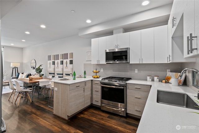 kitchen featuring kitchen peninsula, white cabinets, appliances with stainless steel finishes, dark wood-type flooring, and sink