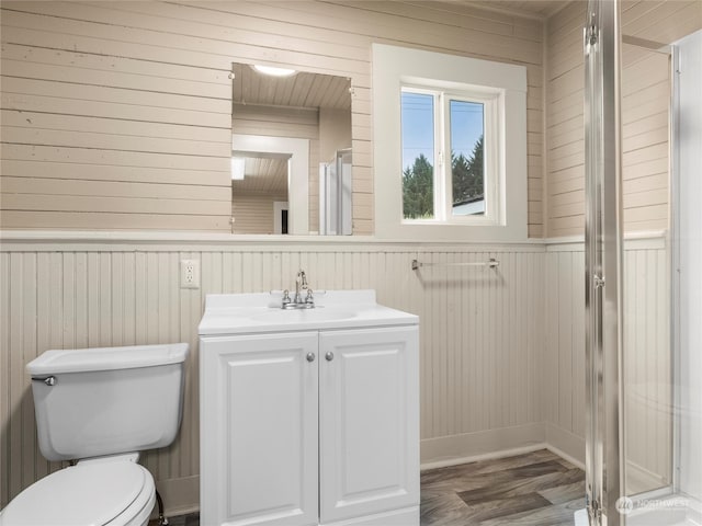 bathroom featuring vanity, wooden walls, hardwood / wood-style flooring, walk in shower, and toilet