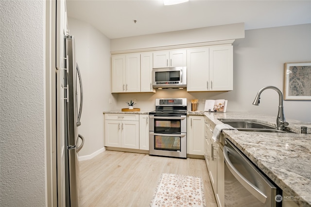 kitchen with light hardwood / wood-style flooring, sink, stainless steel appliances, light stone countertops, and white cabinets