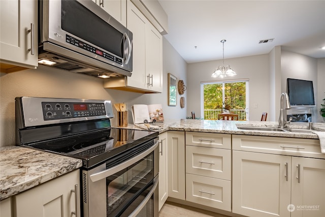 kitchen with light stone counters, sink, kitchen peninsula, appliances with stainless steel finishes, and an inviting chandelier