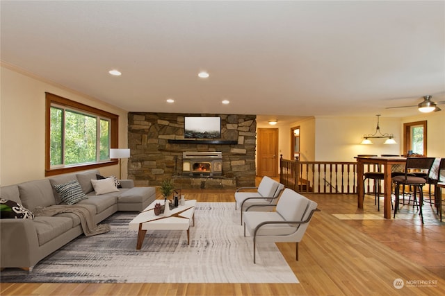 living room featuring light wood-type flooring, a wood stove, ceiling fan, and ornamental molding