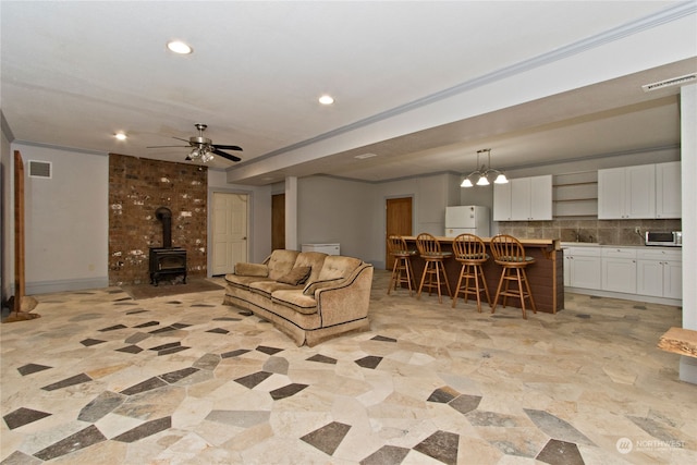 living room featuring ceiling fan, sink, a wood stove, and crown molding