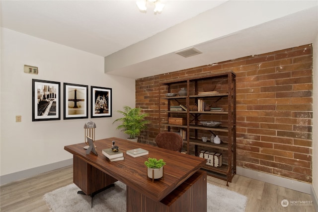 home office with light hardwood / wood-style floors and brick wall