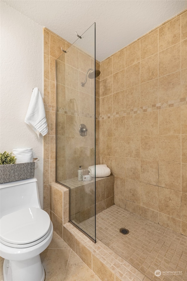 bathroom with a tile shower, a textured ceiling, toilet, and tile patterned floors